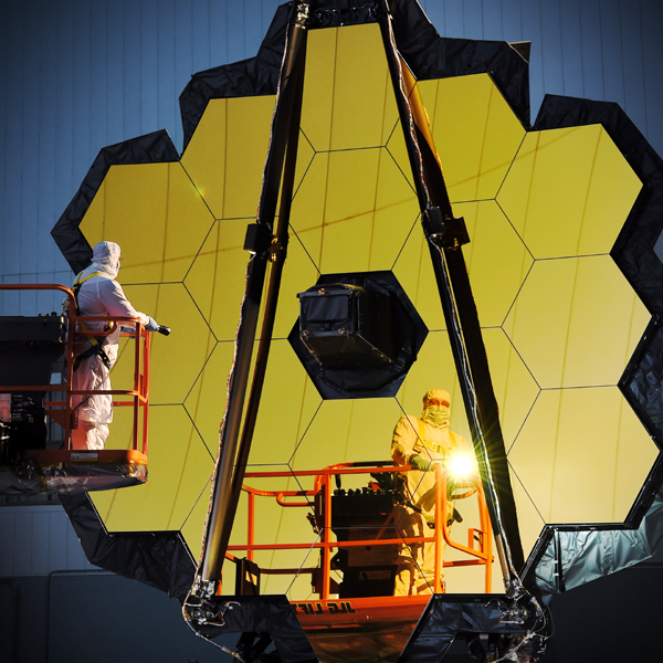 An engineer's reflection is visible on the gold-plated primary mirror of NASA's James Webb Space Telescope. This image was taken well before the spacecraft was shipped to South America for final launch preps.