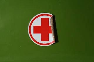 Rotes Kreuz Sticker auf grünem Hintergrund, der sich beginnt abzulösen.