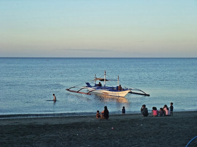 wonderful early morning view of the beach, people hanging around or swimming, with a boat and the sea in the background at Aroma Beach San Jose Occidental Mindoro