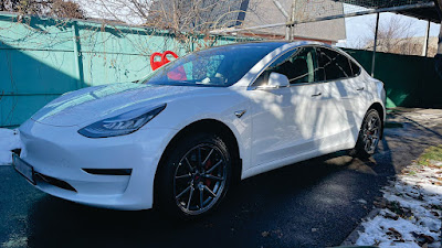 Фото белой Tesla Model 3 Long Range с VIN 5YJ3E1EB1KF361627, стоящей у дома: вид слева под углом.