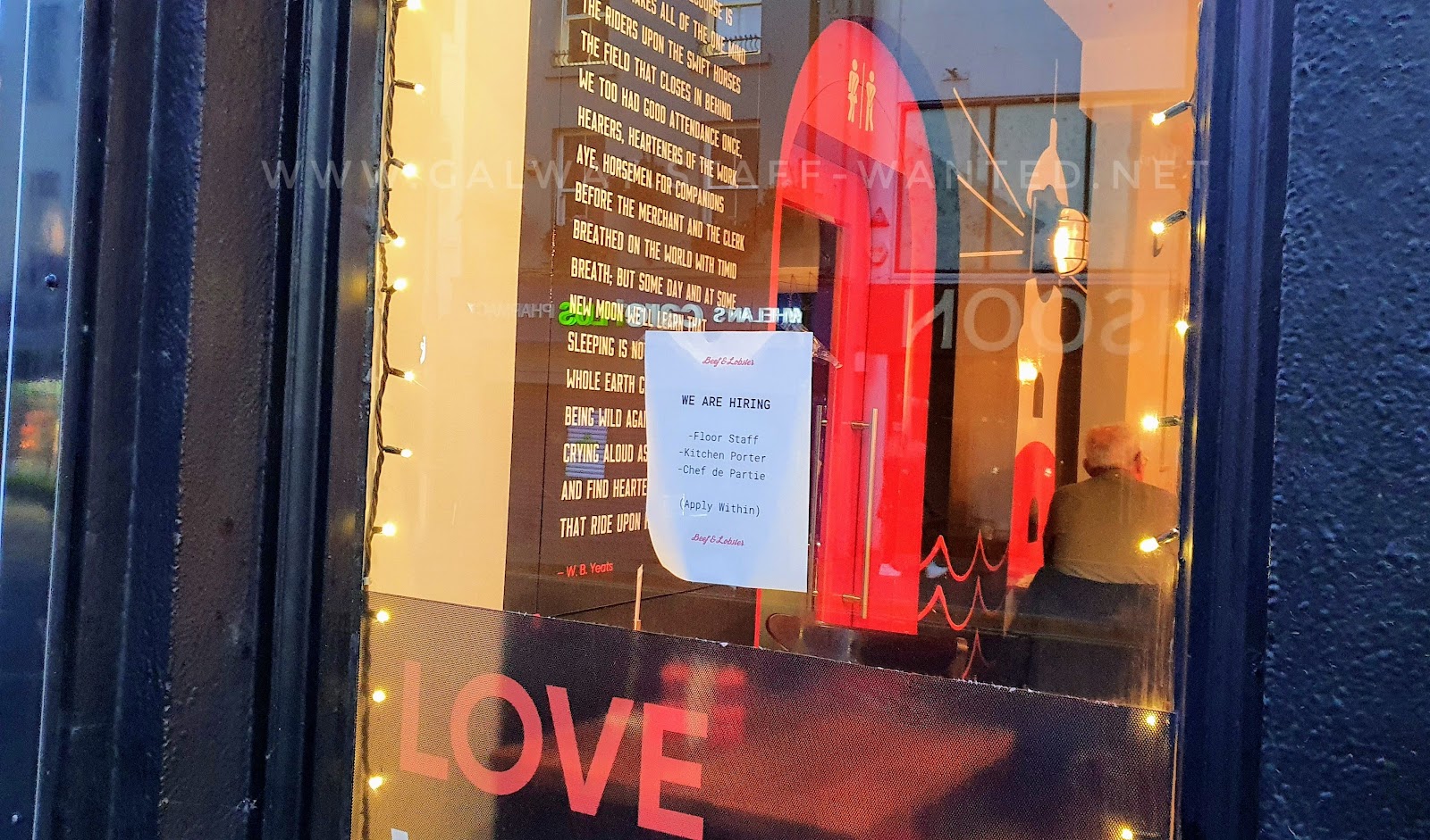 restaurant window with job ad and part of the phrase "love where you eat" - looking to through to wall-to-ceiling poetry and a circular bright red restroom door