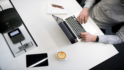 Lone worker in internet marketing work station with a computer, mobile phone, calculator, wallet and a white mug of creamy beverage.