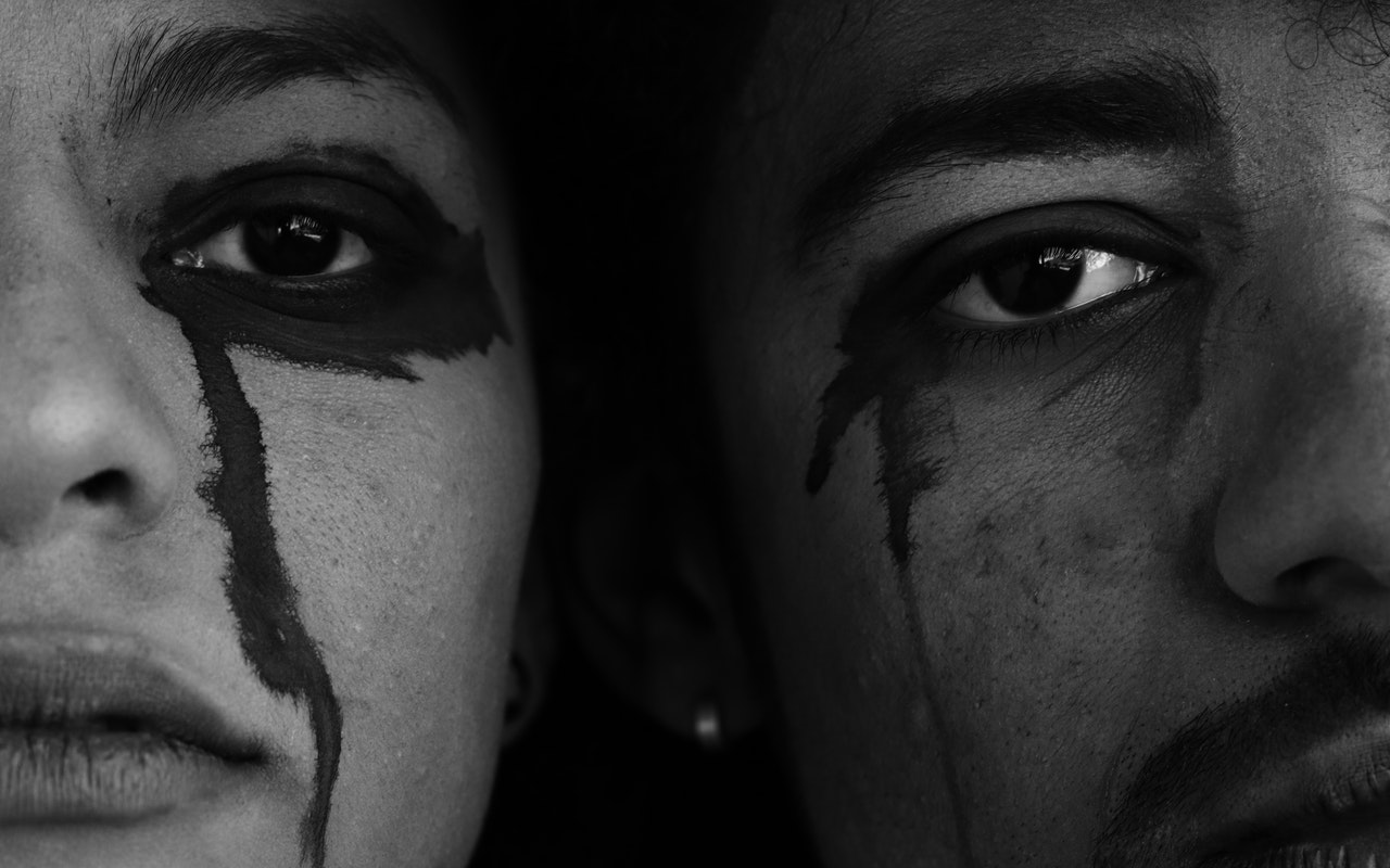 Close up photo of a sad man and a woman lying close to each other. Tears falling down their cheeks are black in colour.