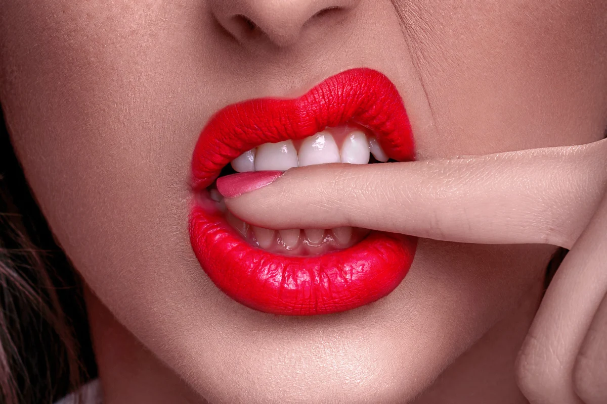 close-up of woman's lips with a red lip color and a finger to her lips