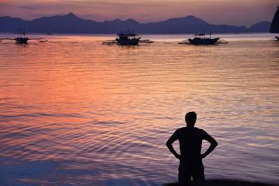 Man stares out at water and sunset with boats and islands