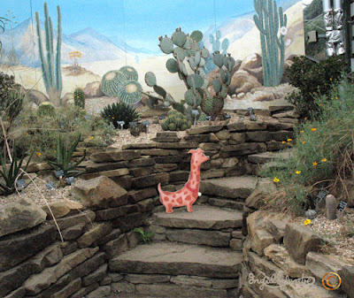 Hals the Neckshund dog at the Secret Portal behind the Intergalactic Cacti The Neckmanns of Giraffe World Storytelling by North East Artist Ingrid Sylvestre at University of Durham Botanic Garden featuring her characters the Neckmanns in their World Artwork and Stories by Ingrid Sylvestre UK Artist & Writer