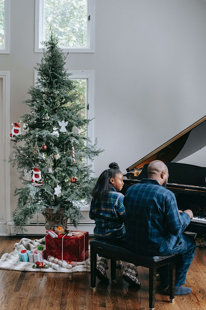 A father and a daughter playing the piano in front of a Christmas tree.