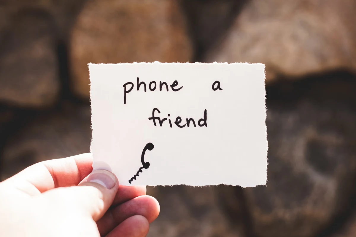 hand is holding a piece of paper with a phrase ''call a friend'' on it