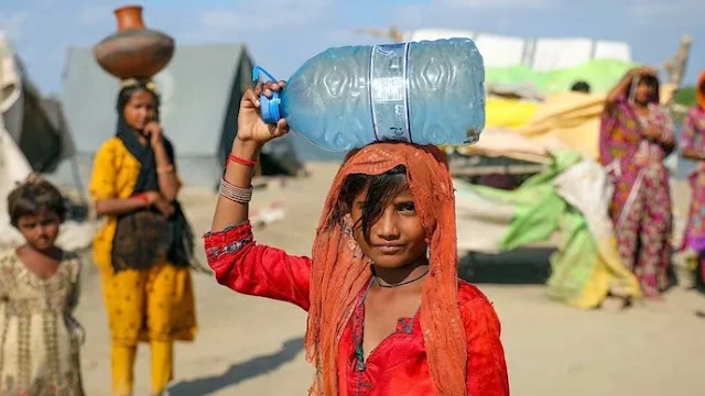 Cover Image Attribute: A file photo of a young girl transporting water obtained from a hand pump in a flooded village located in the Sindh Province of Pakistan. / Source: UN News