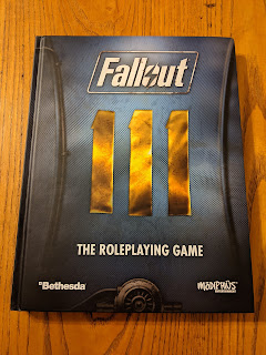 The core rulebook, the cover of which resembles a closeup detail of a section of a uniform from the video game with the insignia that represents the number 111 centred on the cover.