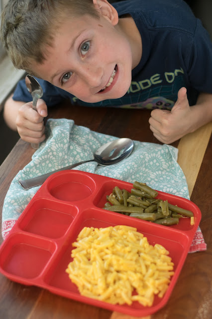 A boy bent over a plate with the green beans giving it a thumbs up.