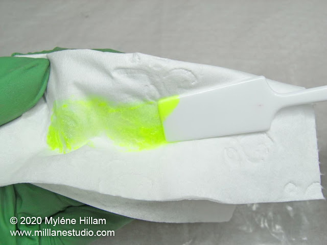 Wiping a smear of yello resin from a plastic spatula across a piece of tissue.