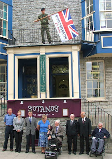 Royal Marine Adam Figgins raising the Armed Forces Day flag at Kitson and Trotmans, observed by members of the Lyme Regis Branch of the Royal British Legion and Kitson and Trotman staff