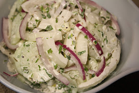 A salad of cucumber and sweet onion, dressed with a creamy, sour cream, mayo and buttermilk herb dressing. Add a little purple onion for color.