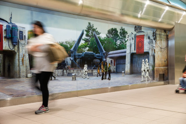 A traveler at Orlando International Airpott in Orlando, Fla., passes by a scene from Star Wars: Galaxy’s Edge at Disney’s Hollywood Studios prior to boarding a shuttle to the Main Terminal, Nov. 16, 2019. Disney installed artistic wraps on the shuttle stations to immerse airport travelers in scenes from Star Wars: Galaxy’s Edge.