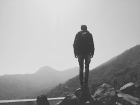 Man standing on top of hill, staring out towards a river and mountains