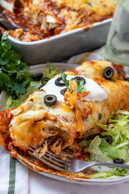 burrito on a white plate with a fork and a piece cut out of it.