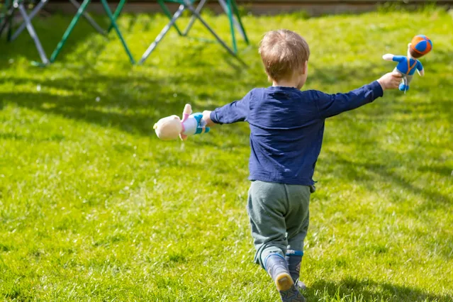 rear view of child running on grass with an Eco Plush toy in each hand
