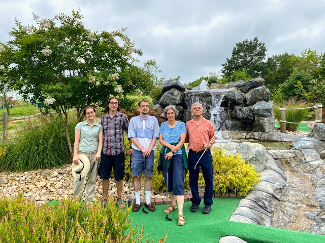 A family smiles on a miniature golf course under cloudy gray skies