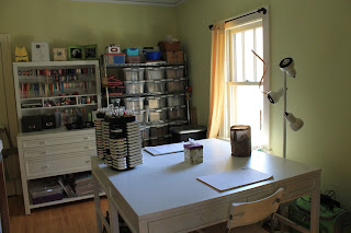 Craft room with new tables, cabinet with hutch and shelves with bins of stamps.