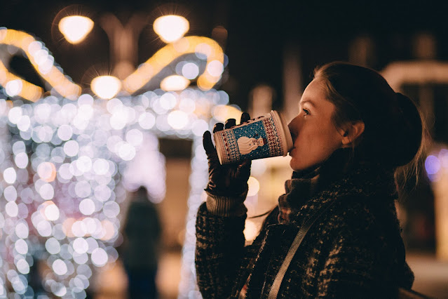 Woman drinking drink outside with background of festive lights:Photo by freestocks on Unsplash