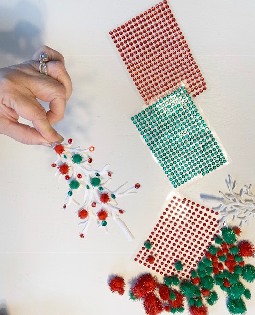 A hand holding a tree ornament decorated with red and green sequins and red and green pompoms