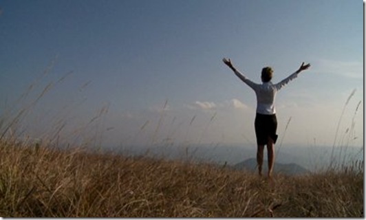 stock-footage-business-woman-standing-on-cliff-s-edge-and-looking-to-a-sky-with-raised-hands