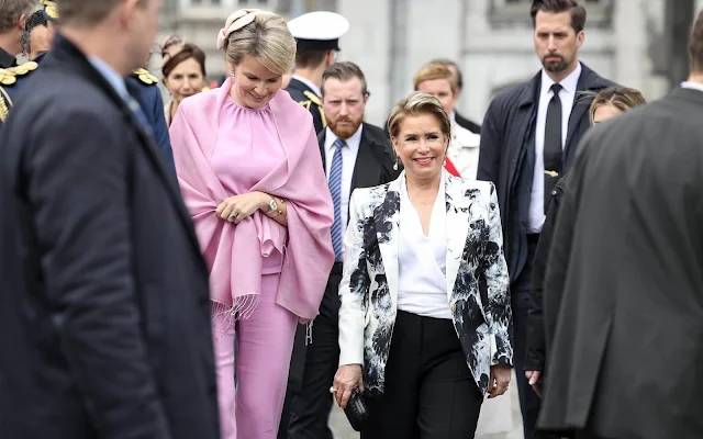 Duchess Maria Teresa wore a Chiaroscuro peak shoulder jacket by Alexander McQueen. Queen Mathilde wore a silk pink top by Natan