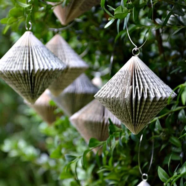 five folded book diamond-shaped paper ornaments displayed on greenery