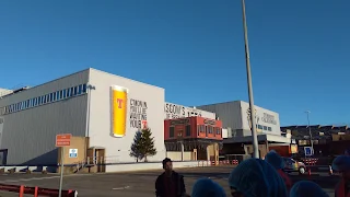 Outside view of a factory. The buildings are light grey and brown. On the light grey building is a painting of a pint of beer and Tennent Brewing Company in red lettering