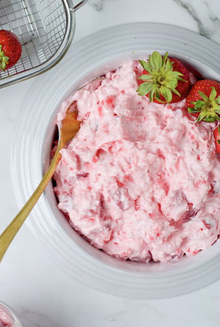 fluff salad in a large bowl with gold spoon and strawberry garnish.