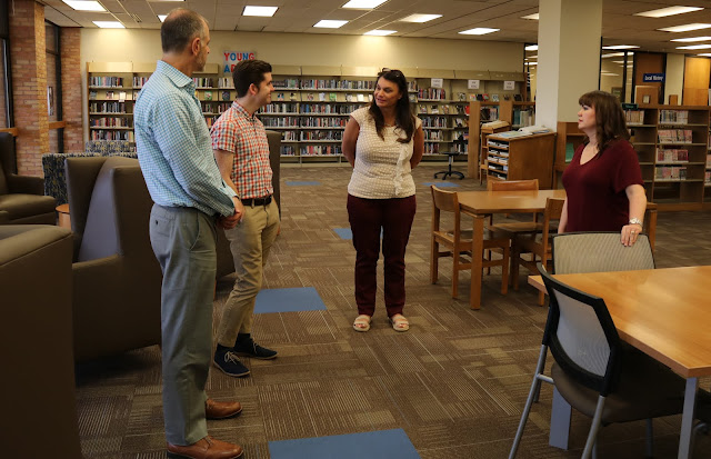 Two men and two women stand in the middle of a library talking