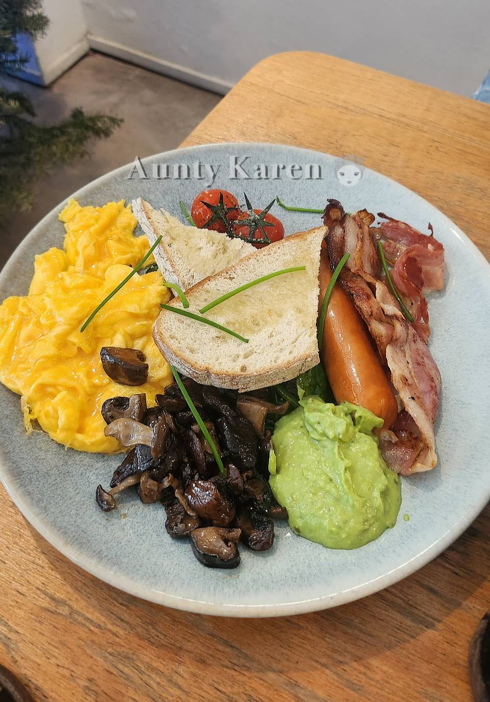 Plate of breakfast food with scrambled eggs, mushrooms, avocado, bacon, sausage, and toast