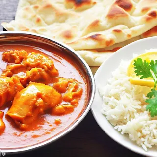 A plate of butter chicken with naan bread and rice, a popular Indian dish