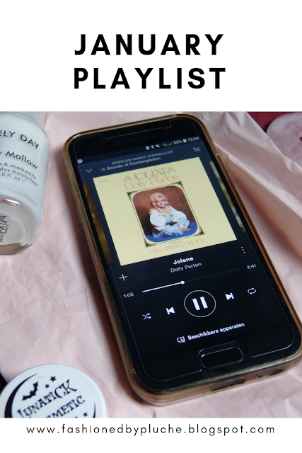 The picture shows a mobile phone with the app Spotify opened, playing Dolly Parton's song Jolene. The mobile is lying on a piece of pink paper. The picture is framed on top and below with white, on it is written "January Playlist" and "www.fashionedbypluche.blogspot.com".