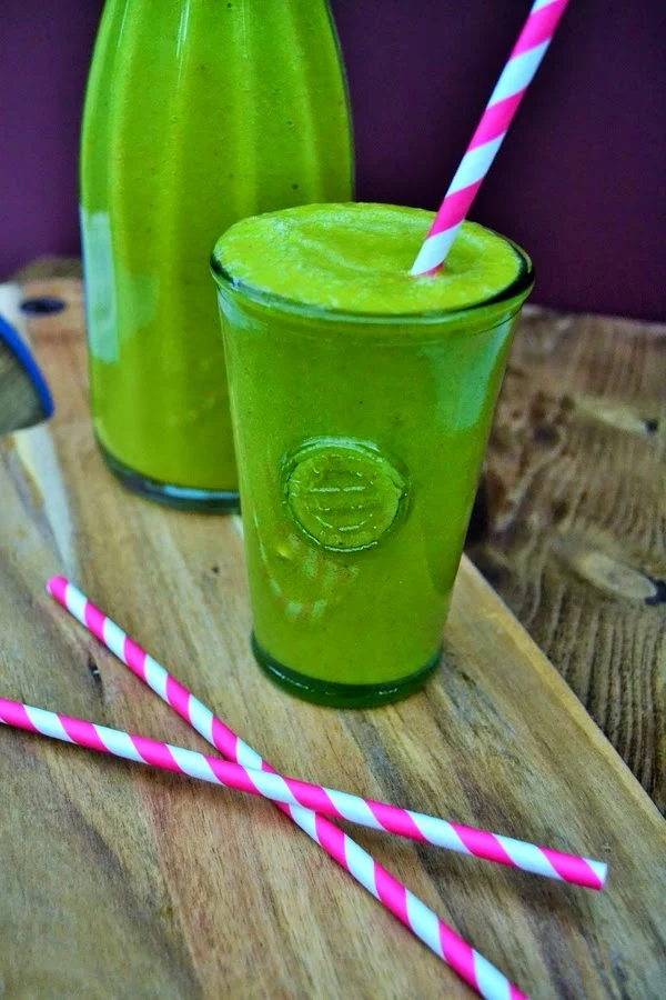 green smoothie in a tall glass with pink and white paper straws