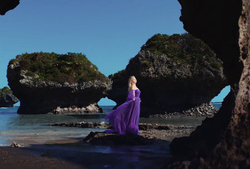 A screenshot of Koda Kumi in her music video for "Silence". Standing outside, wearing a purple dress made of (what looks like) silk and tulle.