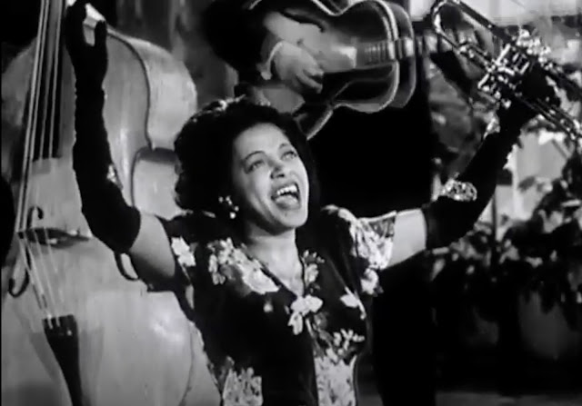 Screenshot from a 1946 Soundie of Valaida Snow singing and holding up her trumpet