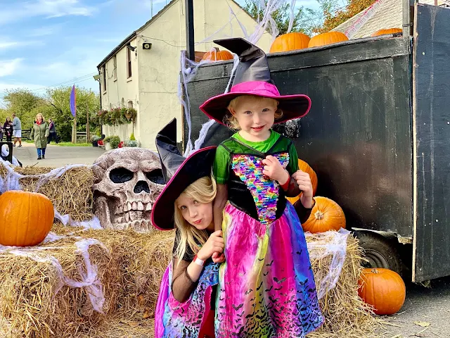 2 sisters dressed as colourful witches in front of a halloween display at Marsh Farm