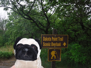 A plush pug appears next to a brown sign that says "Dakota Point Trail Scenic Overlook"  with an arrow pointing up, and a smaller sign below that has an icon of a man hiking.