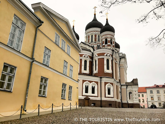 A cobbled lane along a yellow painted three storeyed period house leads to a red brick Russian Orthodox church with four onion domes, under a light grey winter sky.