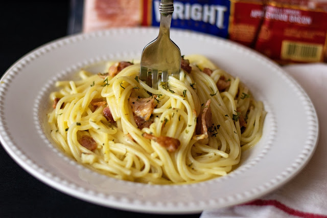 The finished Spaghetti Carbonara in a white bowl, being twirled with a fork.  