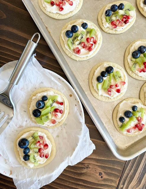 Aerial view of fruit pizza sugar cookies on a sheet pan and plate under parchment paper.