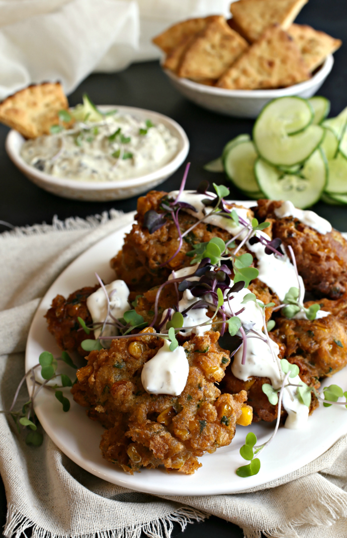 Recipe for savory corn fritters with cheese and herbs, topped with a cucumber yogurt sauce.