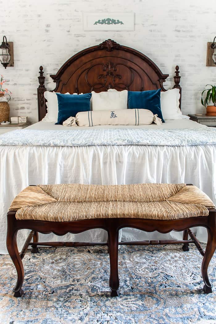 dark mansion headboard, white brick wall, fluffy bed, blue and white pillows, farmhouse bench