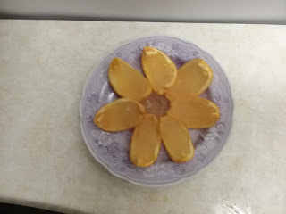 Seven orange slices arranged in a starburst shape on a purple transferware plate. Each slice is a wedge of transparent, almost colorless, jelly set in a section of orange rind.