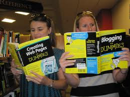 Two girls standing next to each other,reading different books. One reading a book for blogging dummies,and the other reading a book for web dummies.