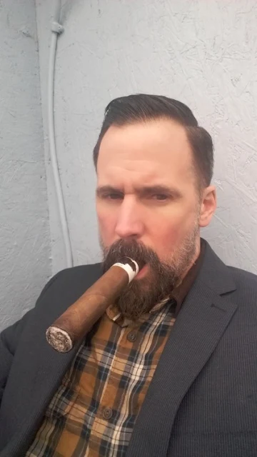 A 2/2 getting back and smoking cigar wearing gray suit flannel shirt underneath bearded good looking man