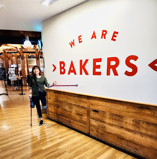 Me, with crutches, standing next to a sign at King Arthur Baking Company that says, "We are Bakers."