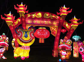 Pic of red Chinese Lantern arch and figures at entrance lit up at night